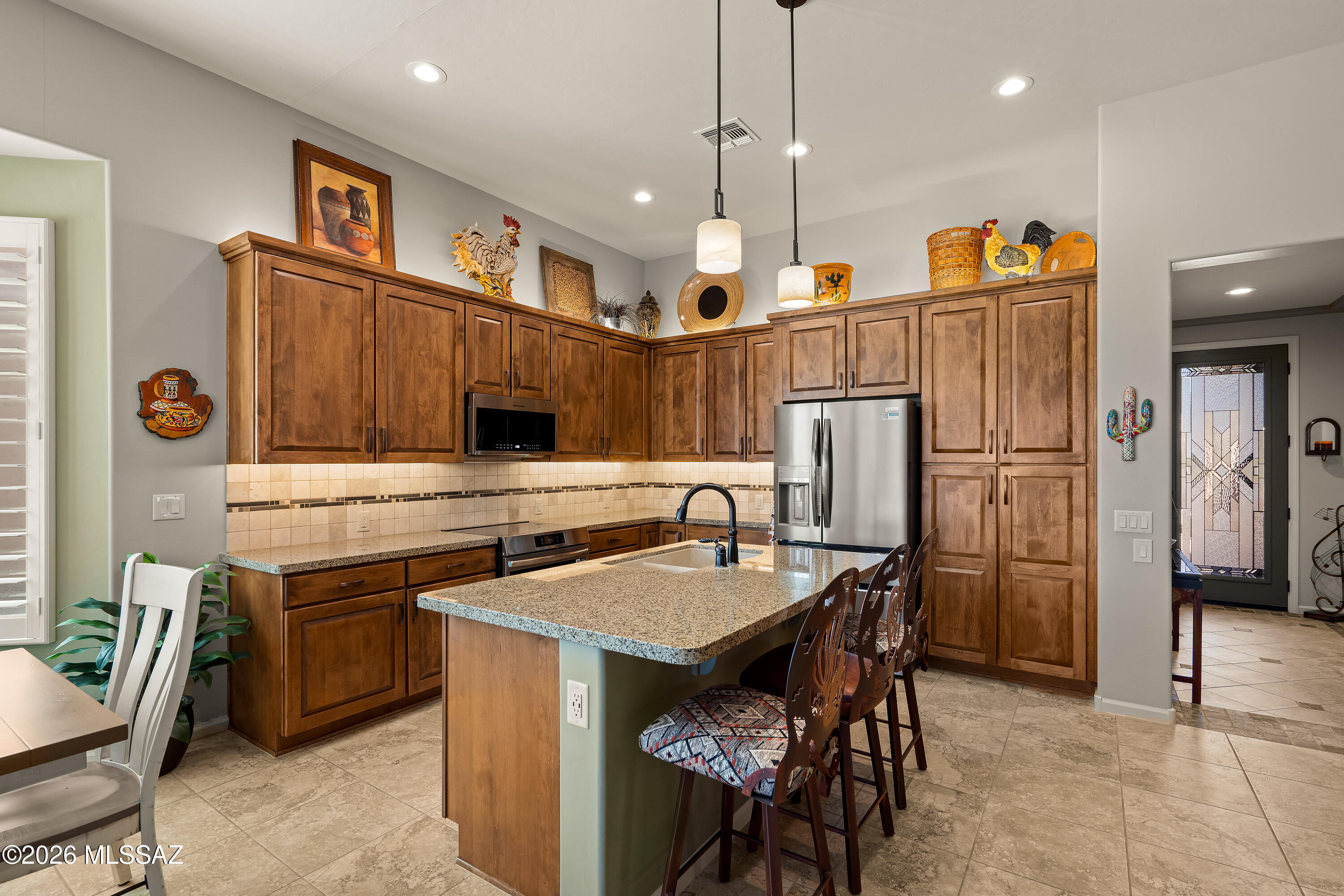 Kitchen with warm wood cabinets, granite island, stainless steel appliances, and bar seating.