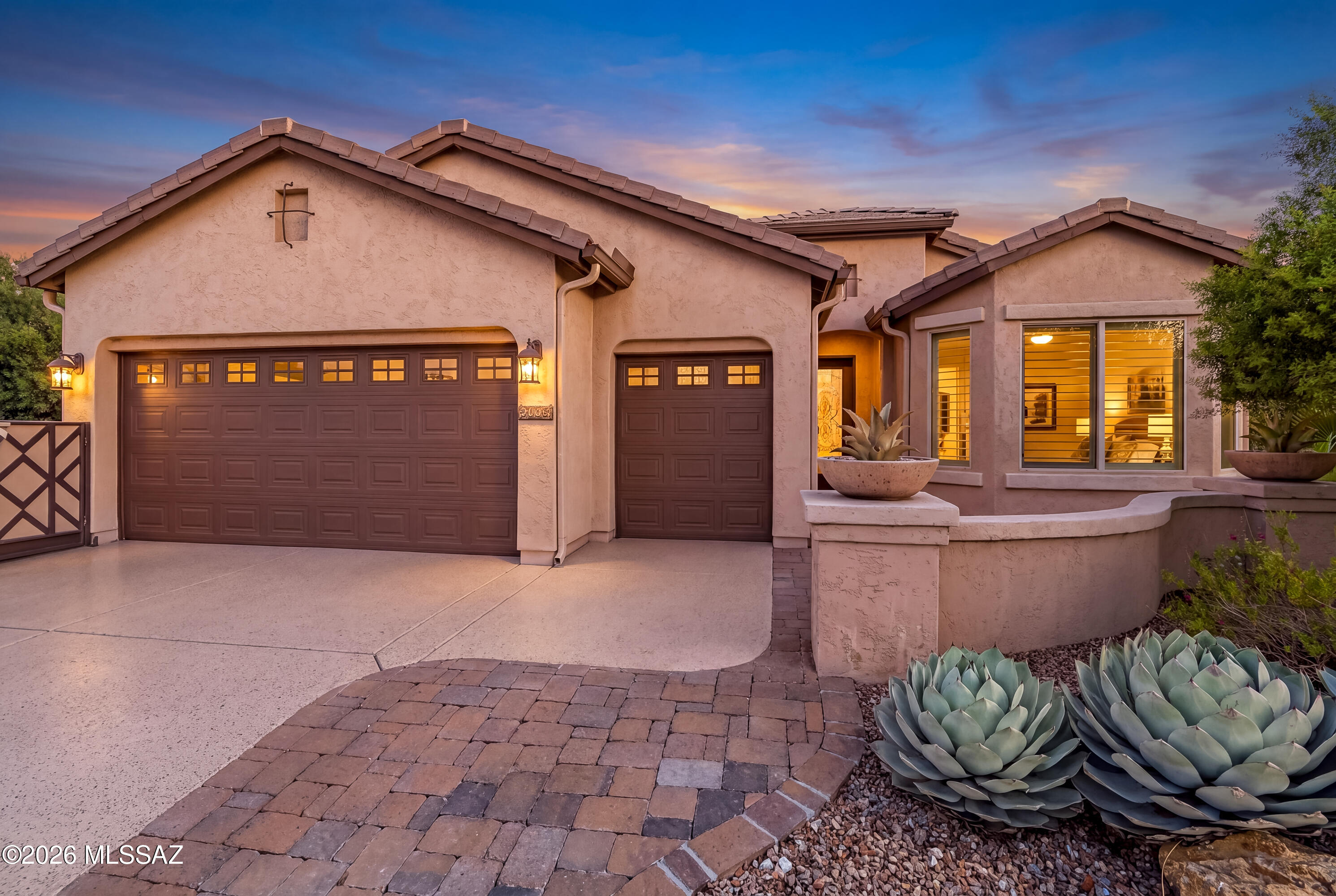 Southwestern stucco home at dusk with two garage doors and large agave plants.
