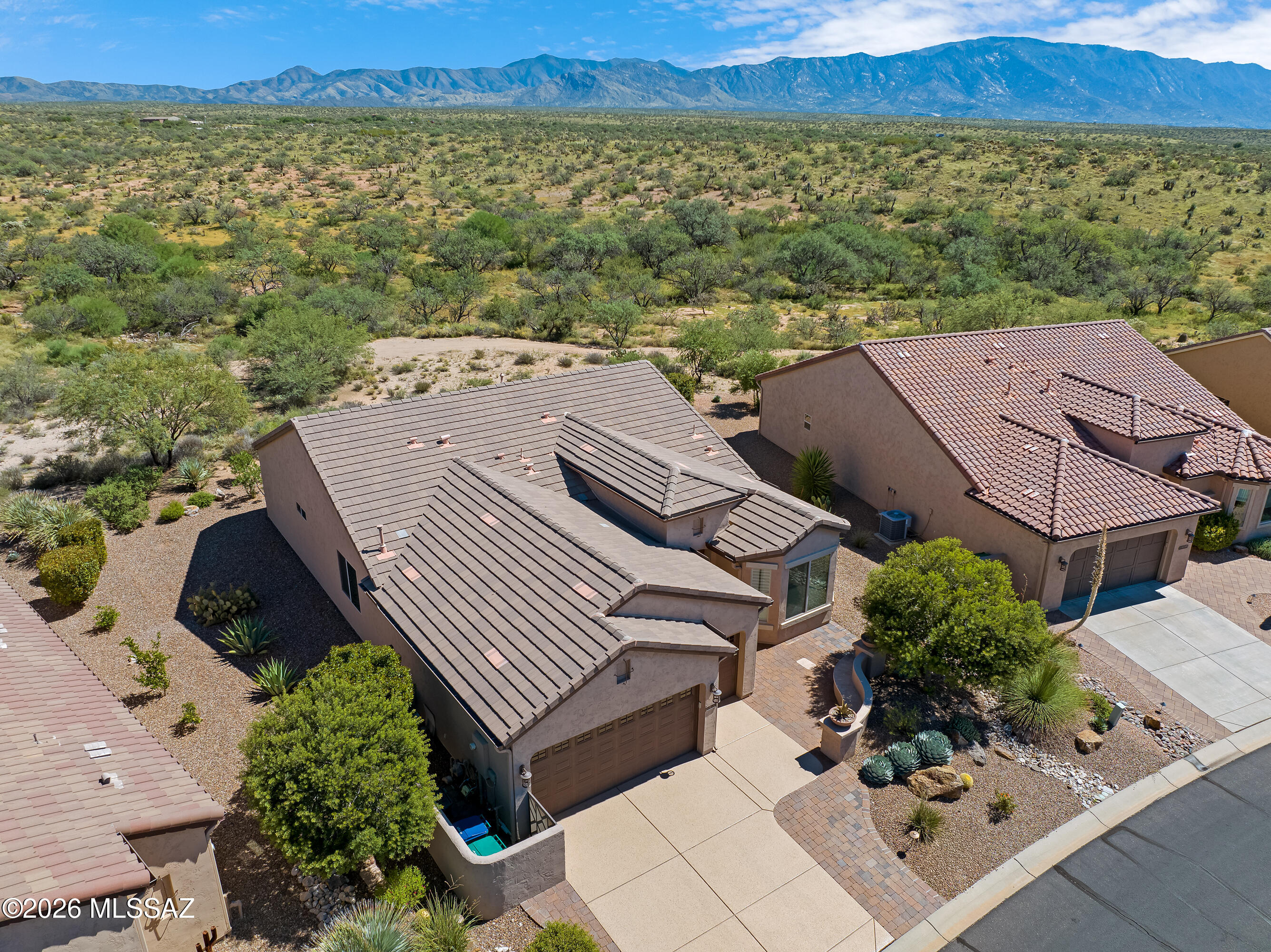 Aerial view of a tan desert home with tile roof, desert landscaping, and mountains beyond.