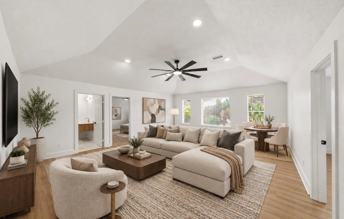 Living room with a vaulted ceiling, large sectional, wood coffee table, and dining area by the windows.
