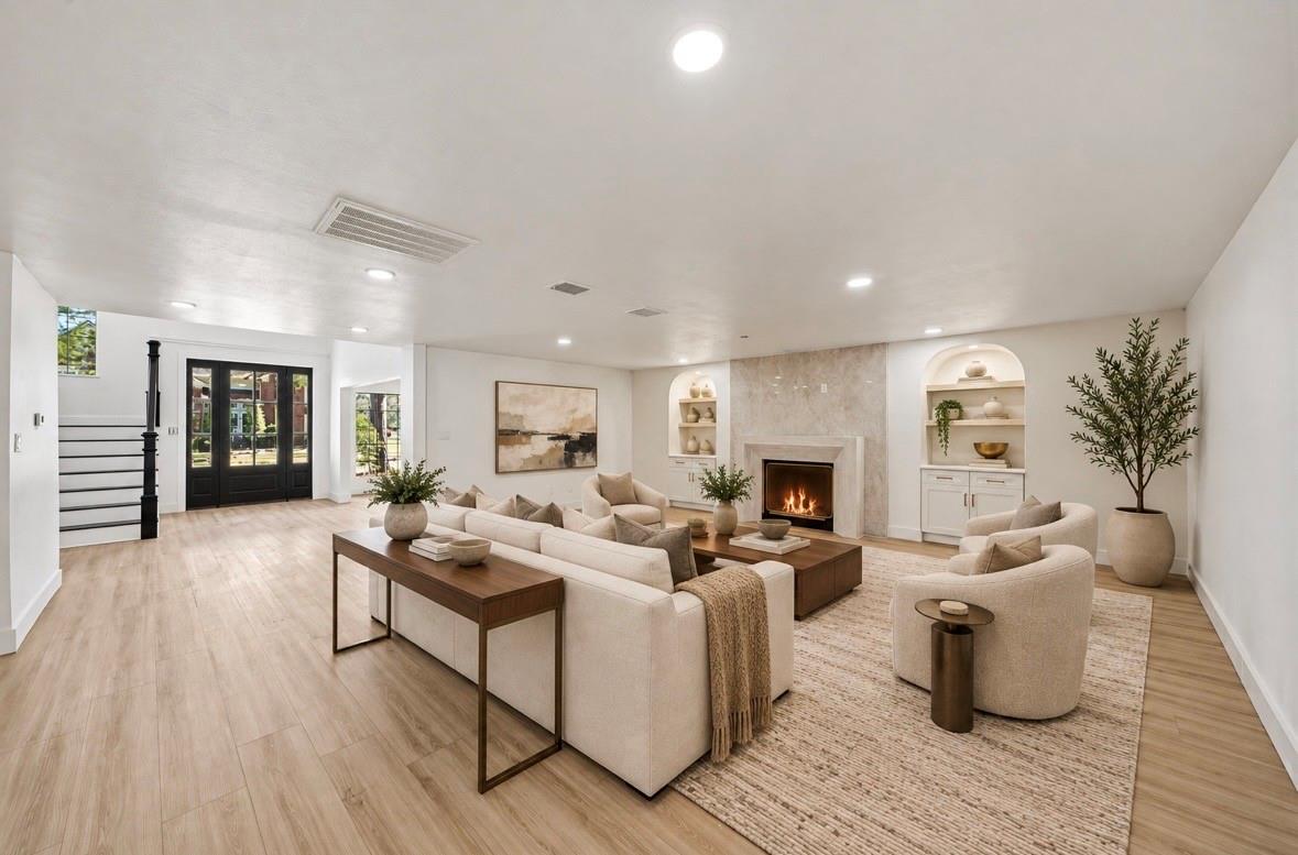 Staged living room with cream seating, a stone fireplace, arched built-in shelves, and black-framed doors.