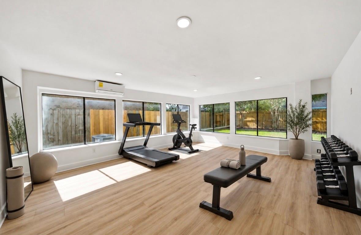 Home gym with treadmill, stationary bike, dumbbell rack, and backyard-facing windows.
