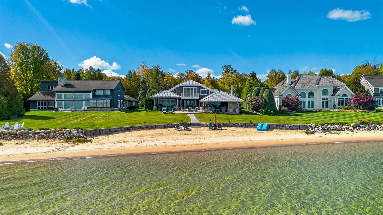 Waterfront homes line a sandy beach beside clear, shallow water.