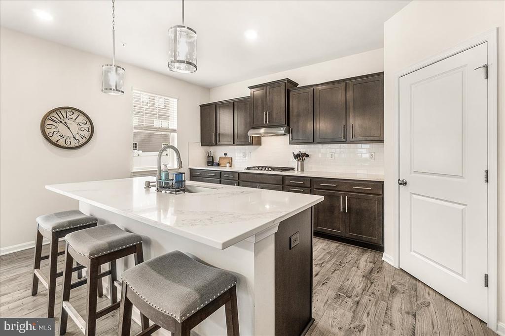 Kitchen with a large white island, three gray stools, and dark wood cabinets.