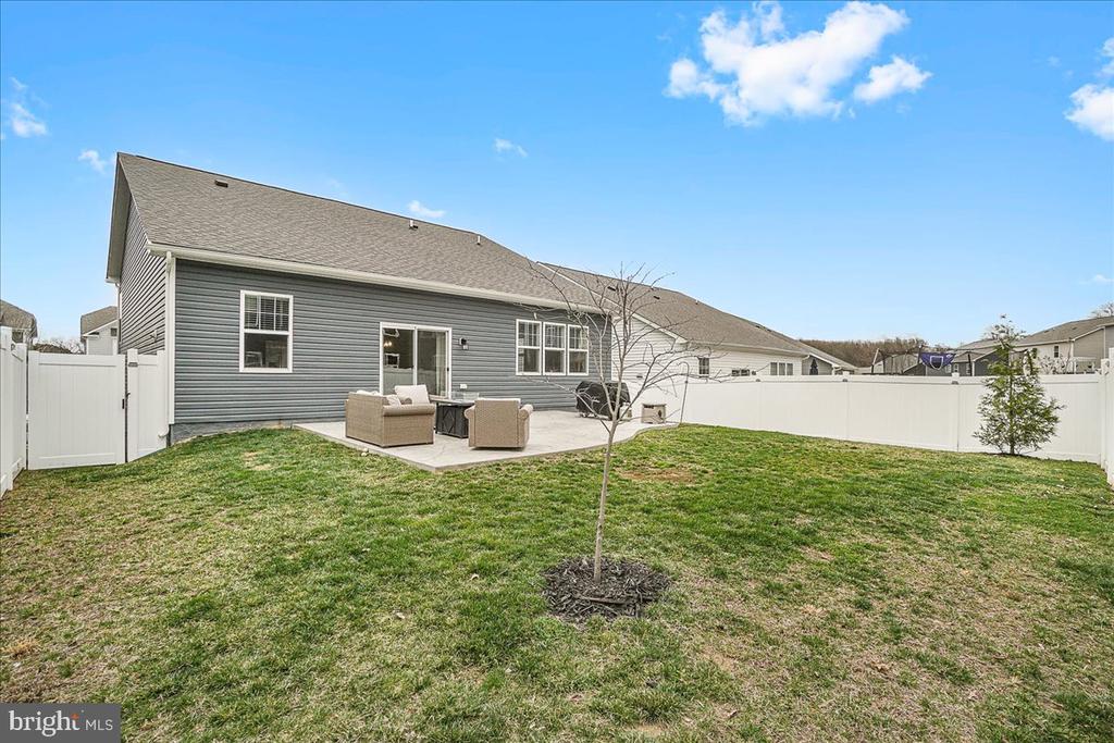 Gray-sided home and fenced backyard with a lawn and patio seating.