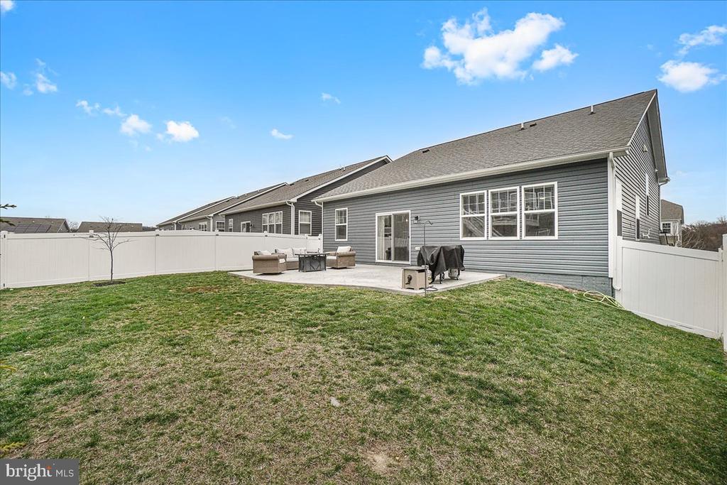 Rear of a gray-sided house with a fenced lawn and concrete patio.