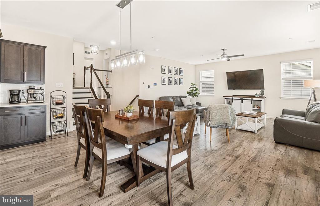 Open-plan dining and living room with a dark wood table, gray sofas, and a staircase.