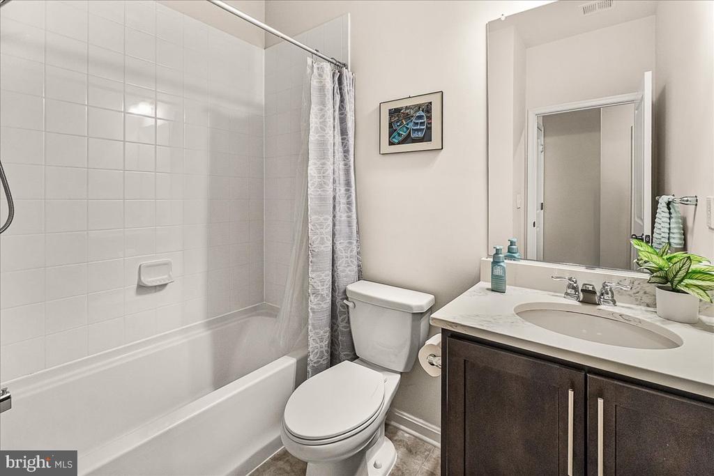 Bathroom with a tiled tub and shower, toilet, and dark wood vanity with an oval sink.