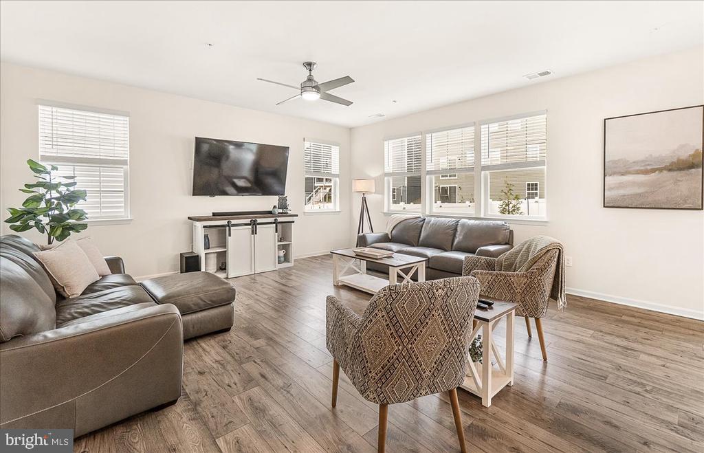 Living room with gray leather seating, patterned chairs, wide windows, and wood-look flooring.