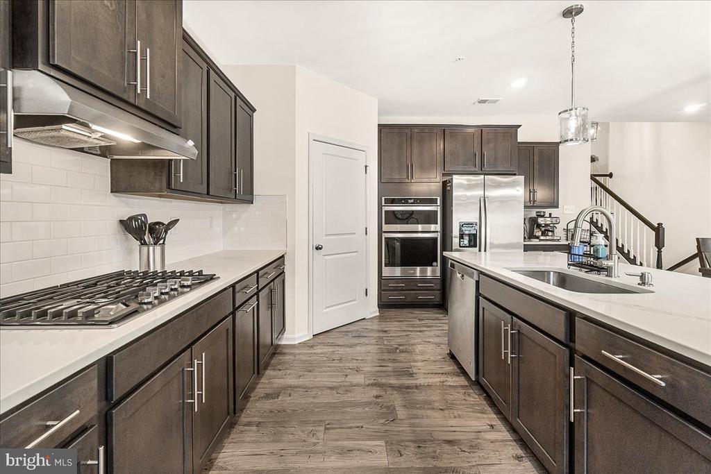 Kitchen with dark cabinets, white countertops, stainless steel appliances, and a large island sink.