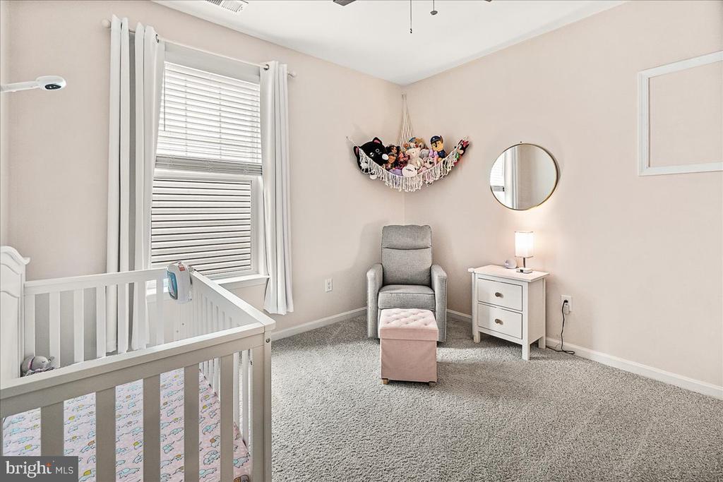 Nursery with a white crib, gray glider and ottoman, plush toys, and a round wall mirror.