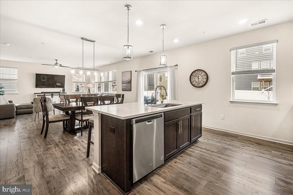 Open kitchen with a large dark island, stainless dishwasher, and adjoining dining and living areas.