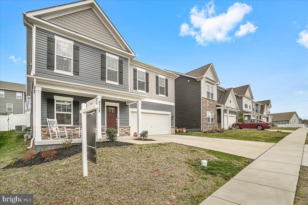 Gray two-story townhouse with a covered porch, attached garage, and neighboring homes along the street.