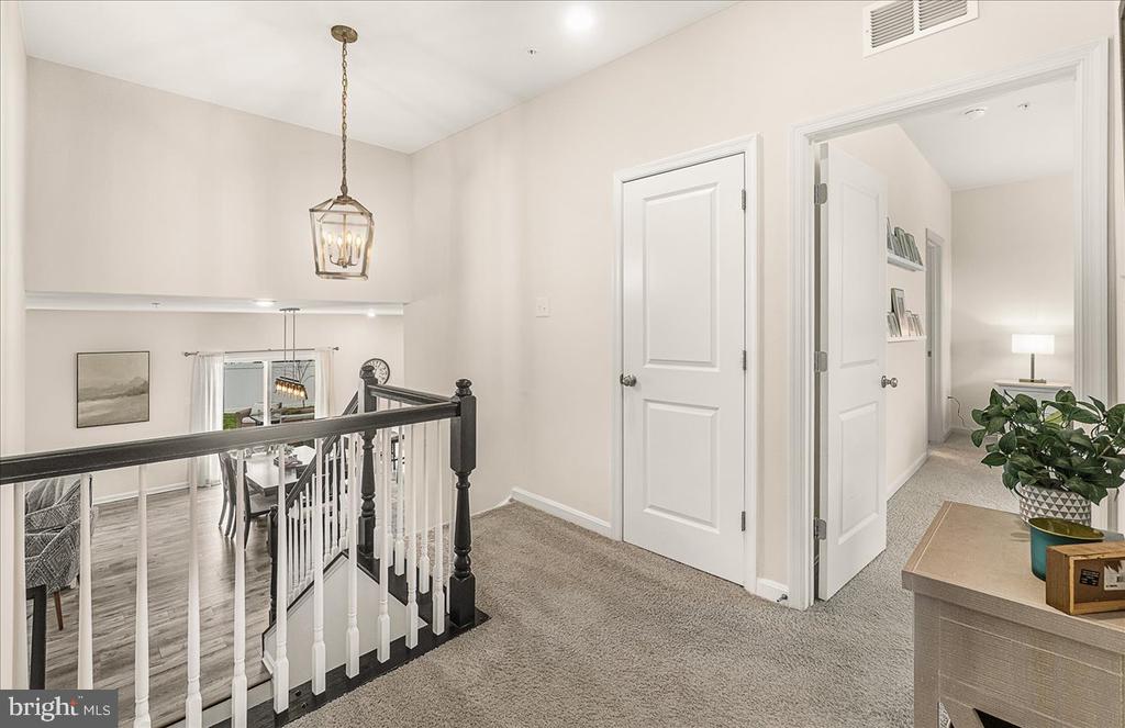 Carpeted upstairs landing with a dark stair railing, white doors, and a console table with a plant.