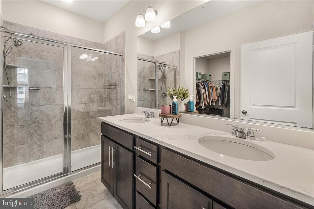 Bathroom with a double-sink vanity and gray-tiled glass shower.