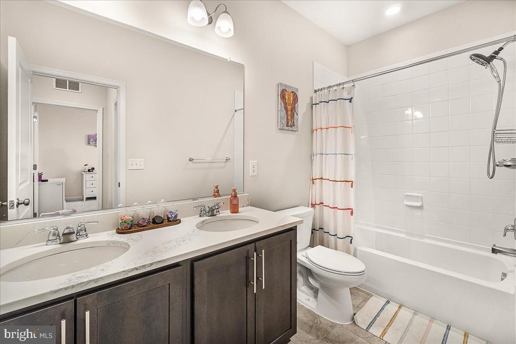 Bathroom with a double vanity, dark wood cabinets, and a white-tiled tub and shower.