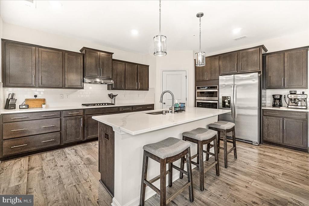Kitchen with dark wood cabinets, stainless steel appliances, and a large white island with stools.
