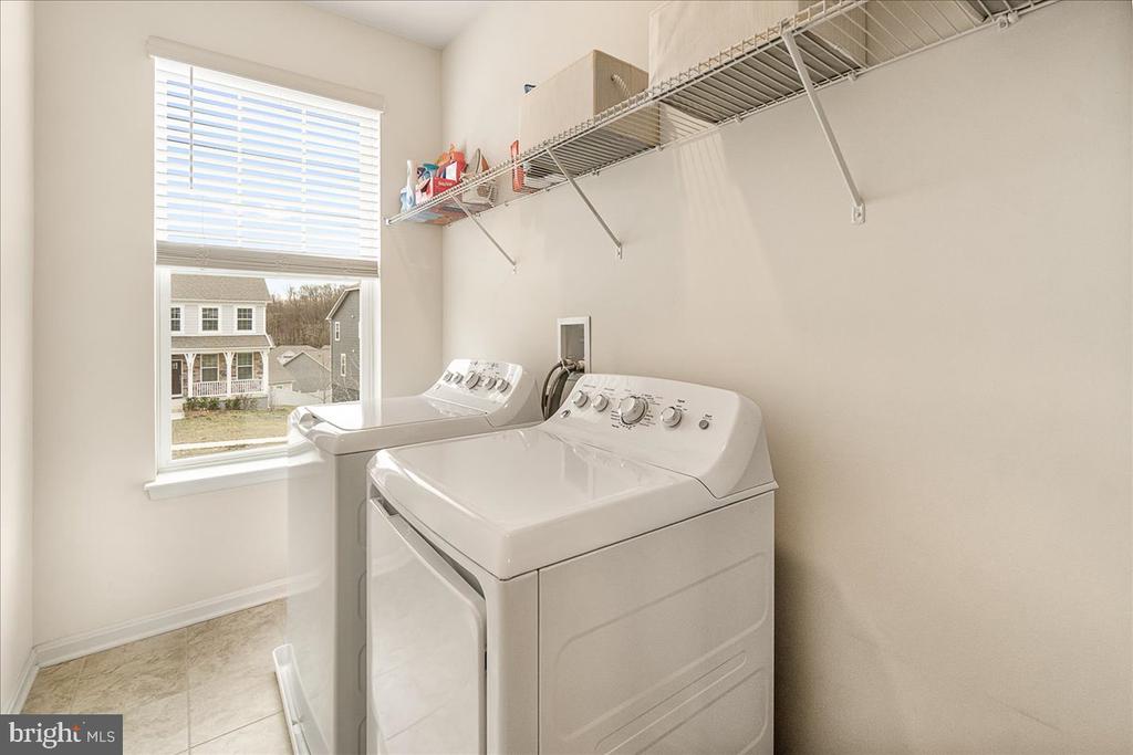 Laundry room with white washer and dryer, wire shelf, and a window overlooking neighboring homes.