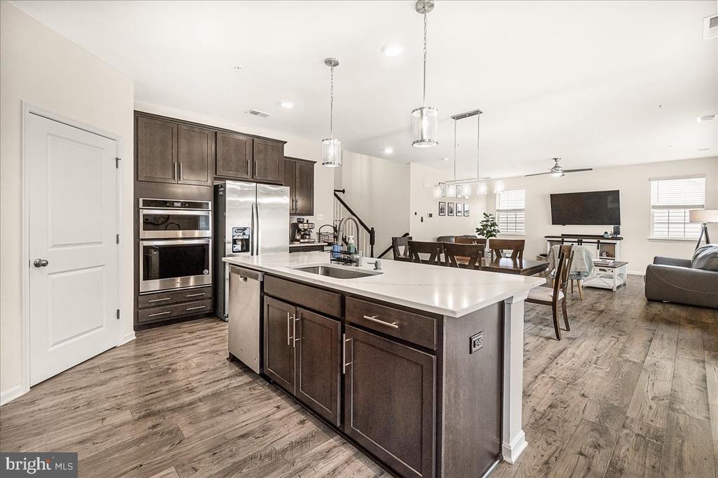 Open kitchen with a large white island, dark cabinetry, and stainless steel appliances.