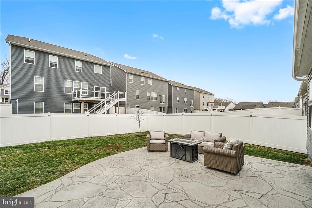 Backyard patio with stone paving, wicker seating, lawn, and white privacy fence.
