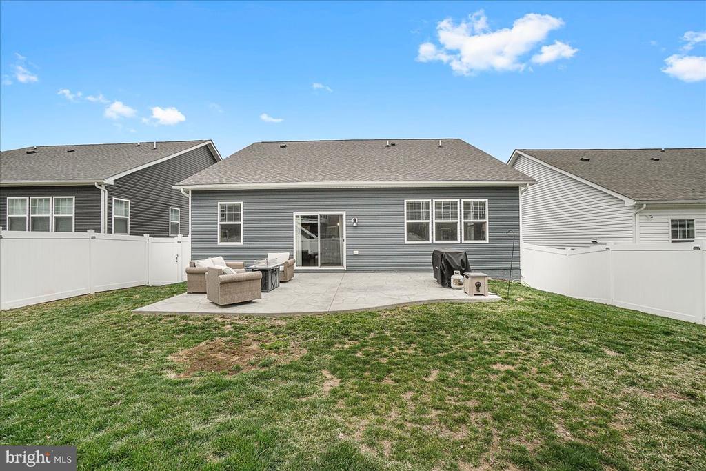 Gray-sided home with a fenced backyard and paved patio furnished with chairs and a grill.