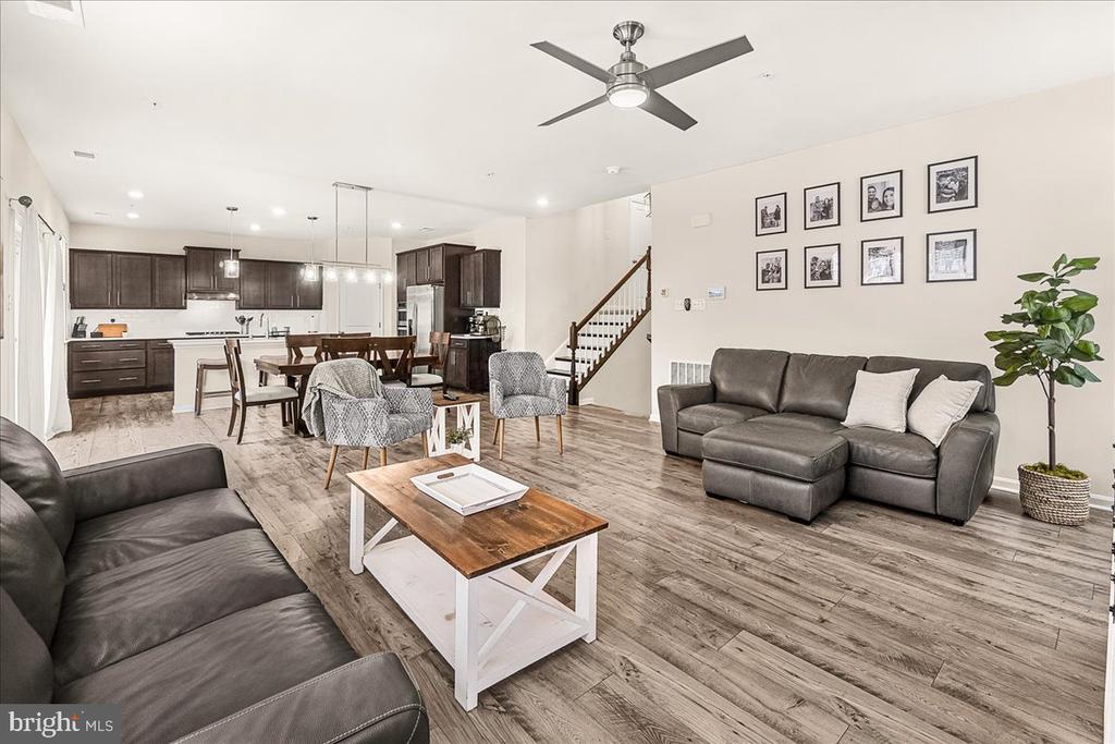 Open-plan living room with gray sofas, wood coffee table, dining area, and dark-cabinet kitchen.