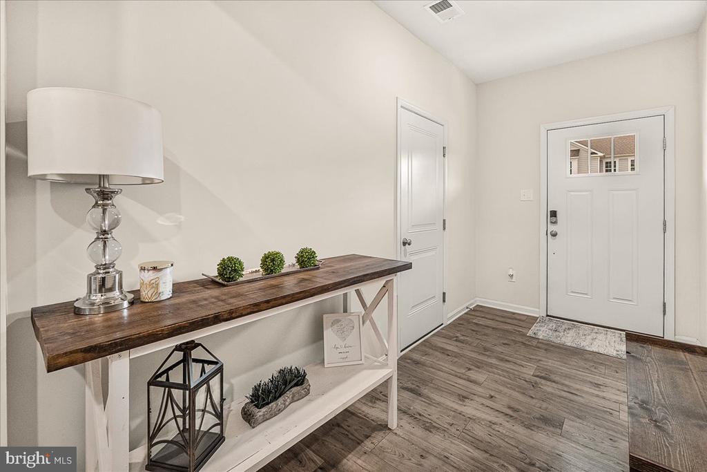 Staged entryway with a dark wood console table, decorative plants, and a white front door.