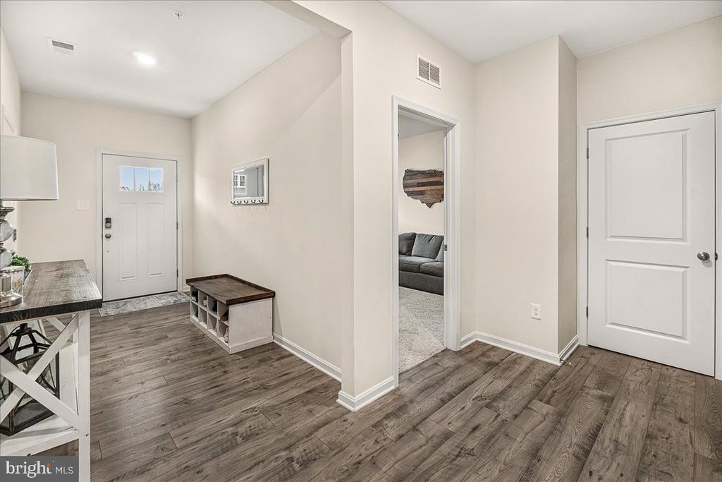 Entry foyer with wood-look floors, a white front door, storage bench, and view into a living room.