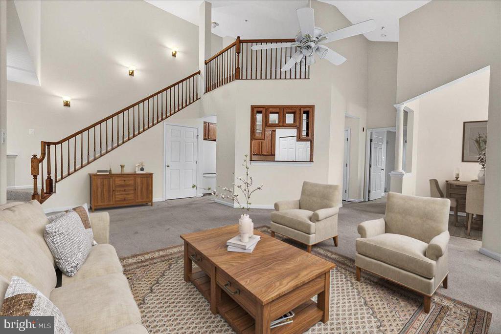 Two-story living room with a wooden staircase, ceiling fan, and beige seating around a coffee table.