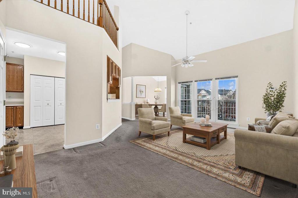 Two-story living room with vaulted ceiling, open staircase, and tall windows overlooking neighboring homes.