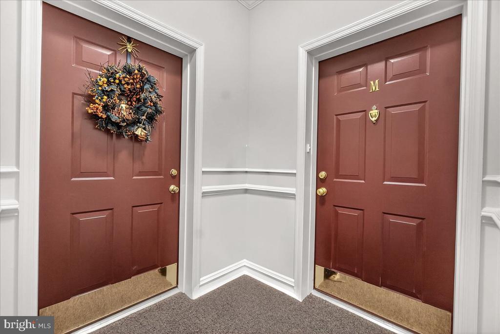 Entryway with two burgundy doors, one displaying a colorful wreath, and detailed white trim.