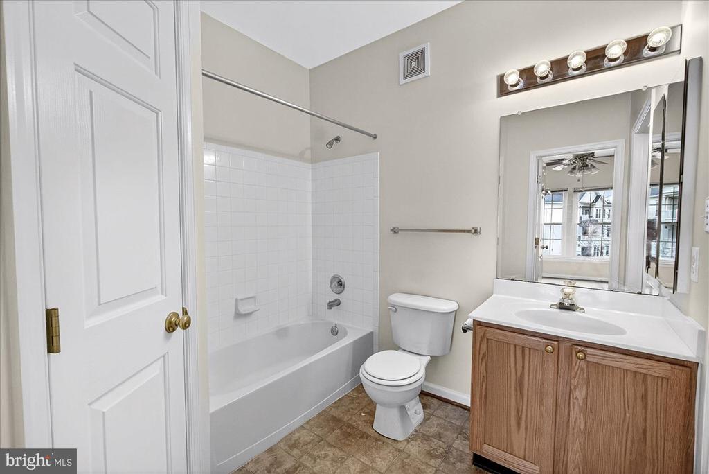 Bathroom with a white tub and shower, toilet, and wood vanity.