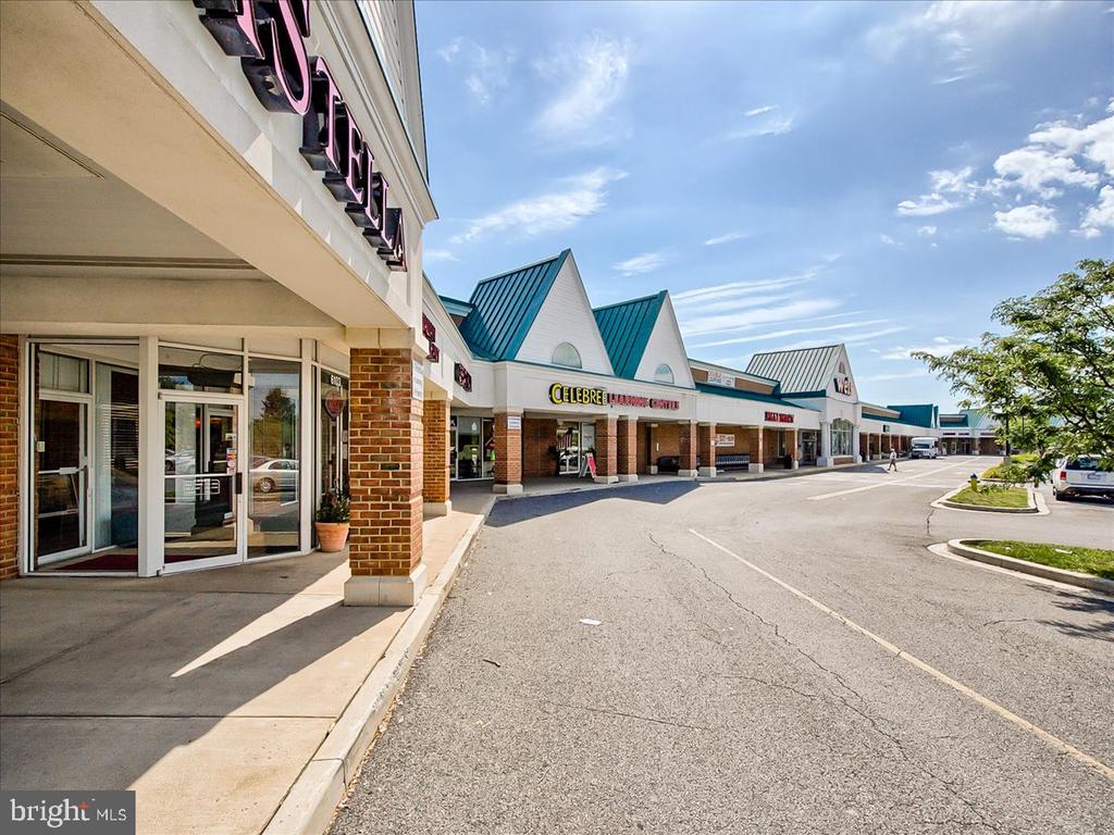 Shopping center with brick storefronts, teal gabled roofs, and a paved lane.