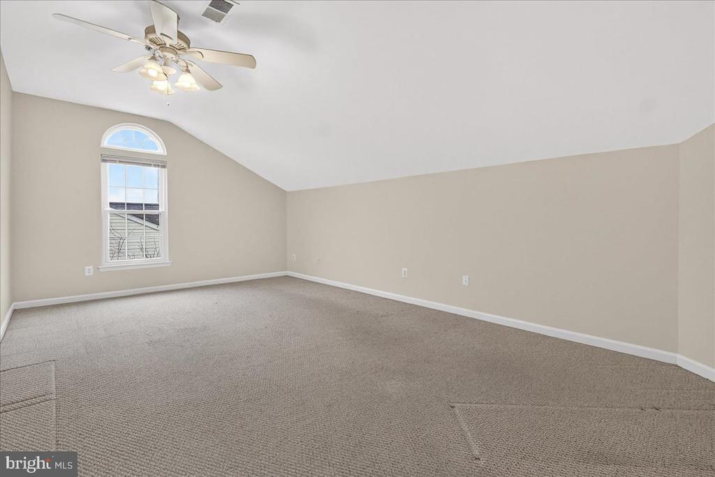 Empty carpeted bedroom with a vaulted ceiling, arched-top window, and ceiling fan.