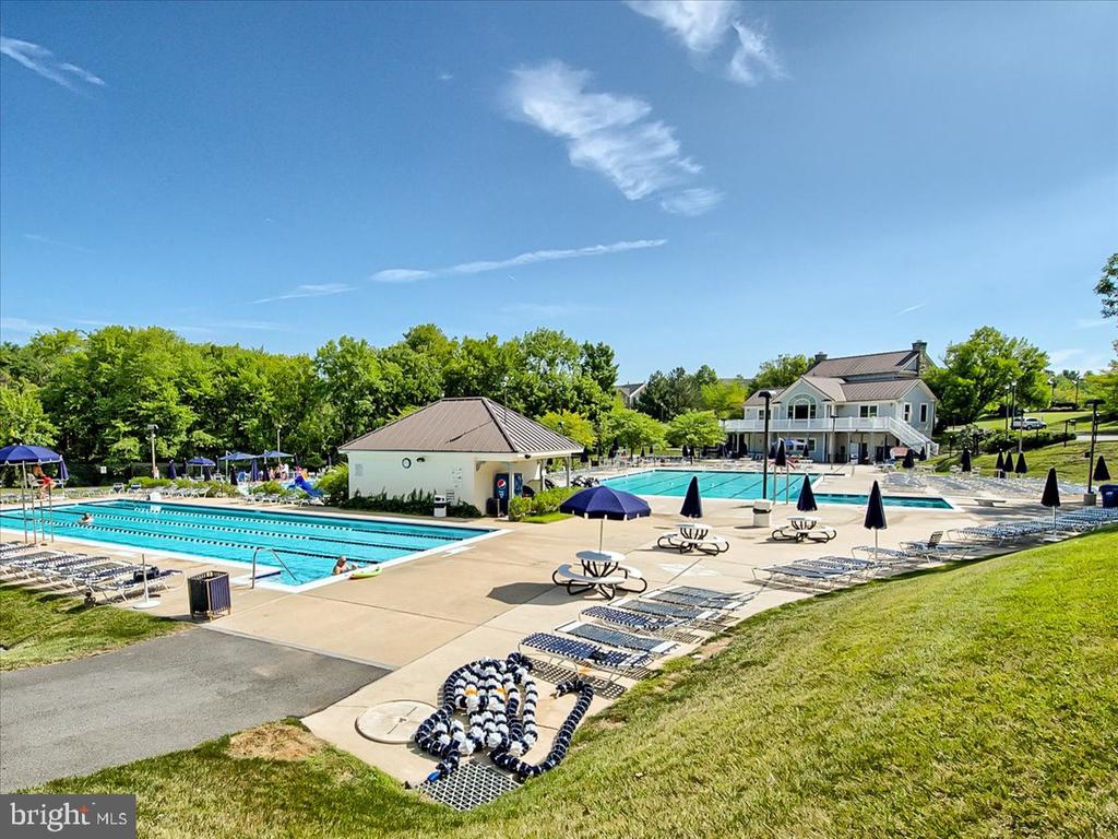 Community swimming pools with lap lanes, a clubhouse, umbrellas, and lounge chairs.