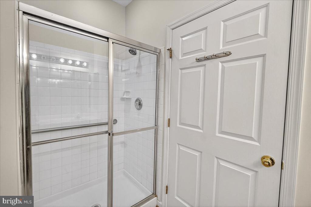 White tiled shower with a sliding glass enclosure beside a paneled bathroom door.