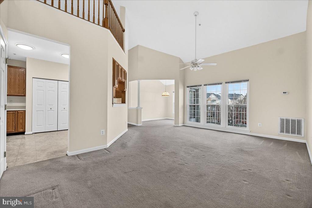 Empty vaulted living room with tall windows, a ceiling fan, and an upstairs railing.