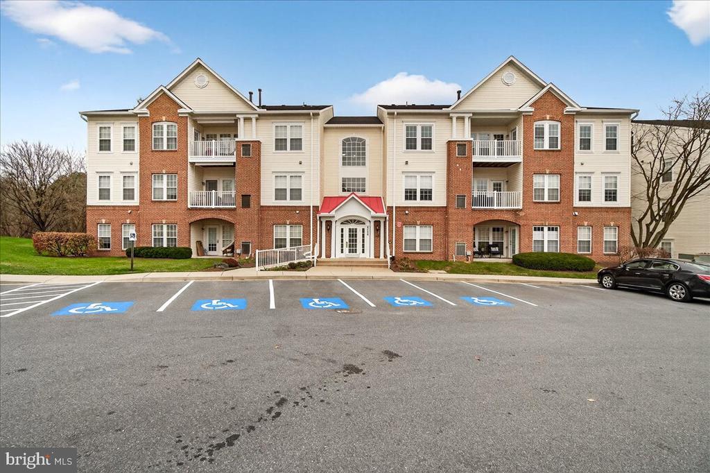 Three-story apartment building with brick and siding, balconies, and accessible parking in front.