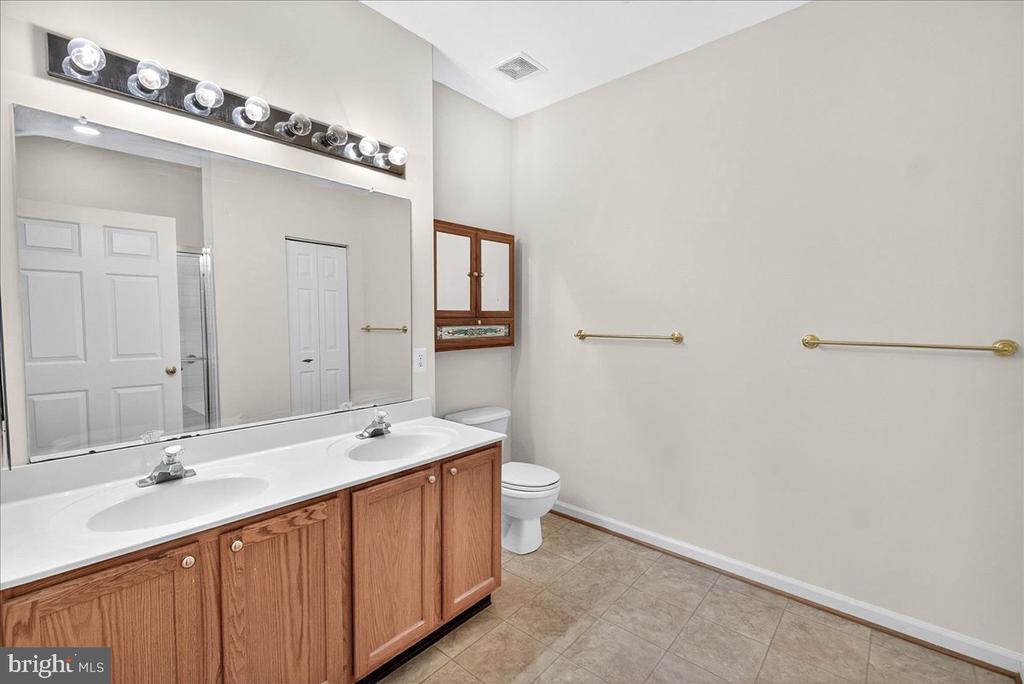 Bathroom with a double-sink wood vanity, large mirror, and tiled floor.