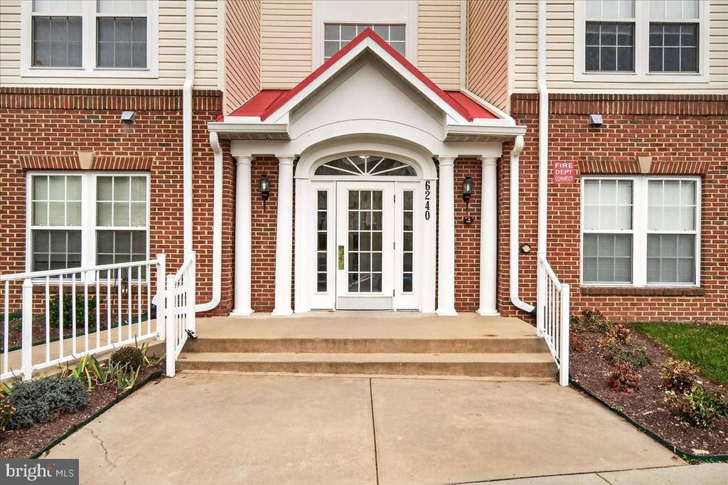 Residential building entrance with a brick facade, red-trimmed portico, and white railings.