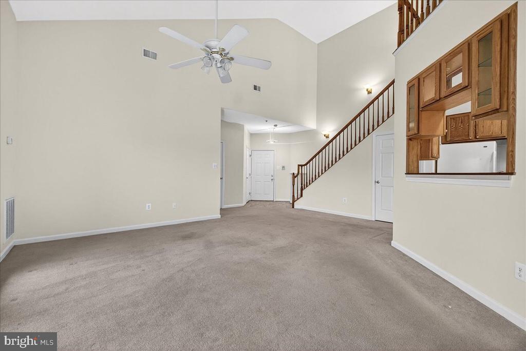 Empty carpeted living room with a high ceiling, wooden staircase, and built-in cabinetry.
