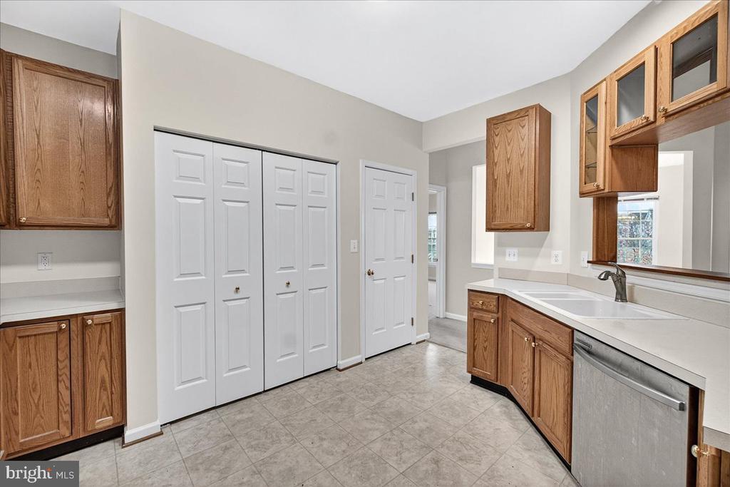 Kitchen with oak cabinets, white counters, gray tile floors, and a stainless-steel dishwasher.