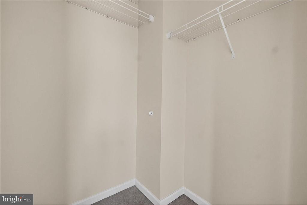 Empty closet with white wire shelving along two walls and gray carpet.