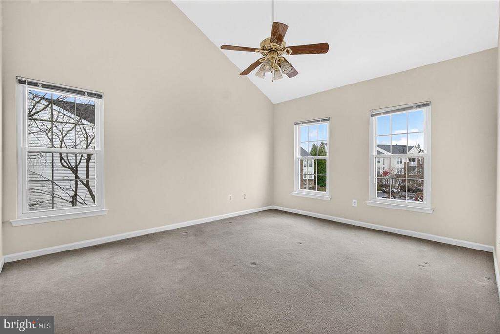 Empty carpeted bedroom with three windows and a ceiling fan.