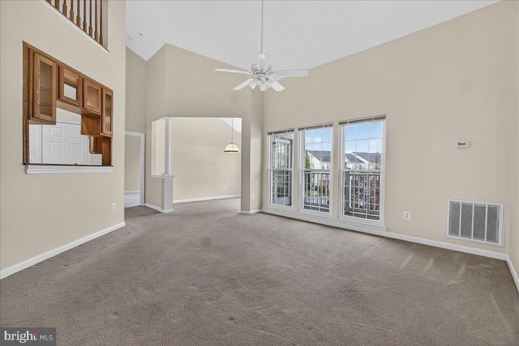 Vacant living room with vaulted ceiling, carpet, ceiling fan, and glass doors to a balcony.
