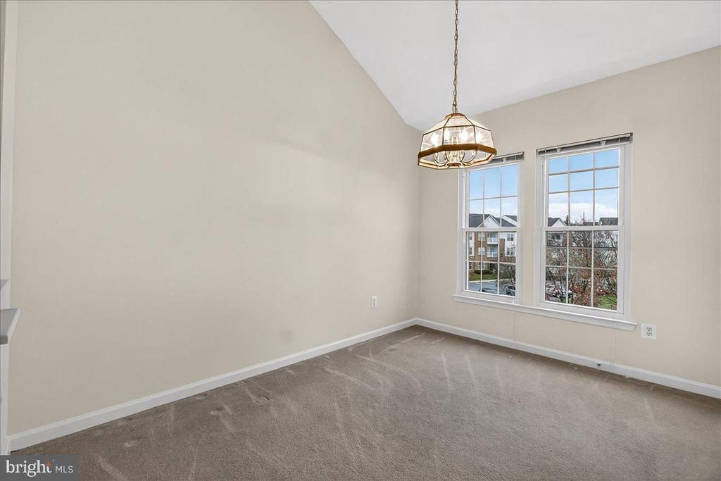 Vacant room with beige carpet, a hanging light, and two tall windows.
