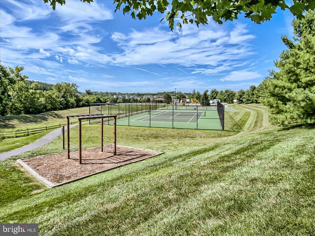 Community tennis court beside grassy slopes and a wooden play structure.