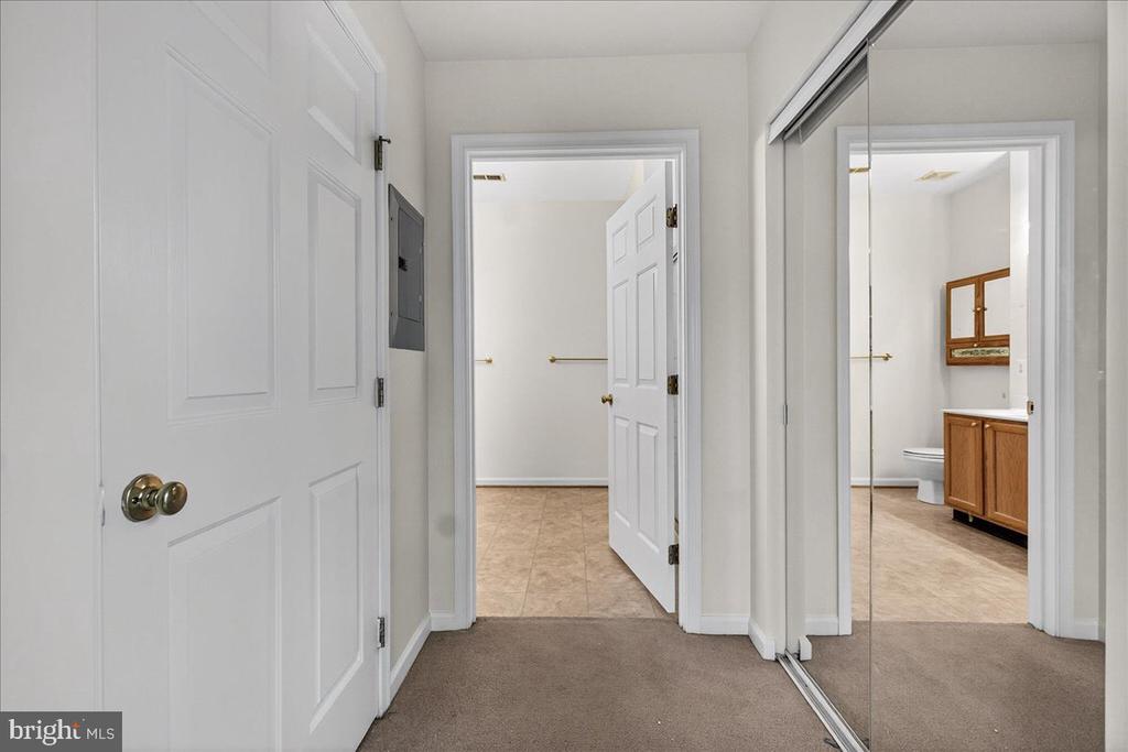 Carpeted hallway with mirrored closet doors and a view into a bathroom with a wood vanity.