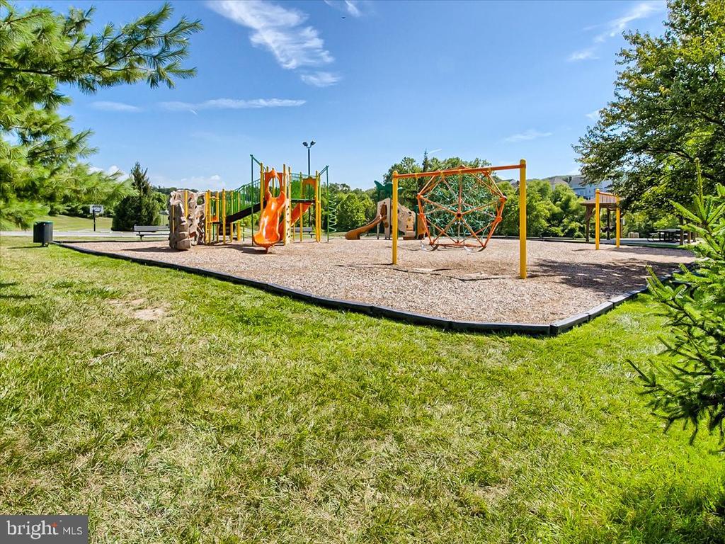 Community playground with colorful slides and climbing structures surrounded by grass and trees.