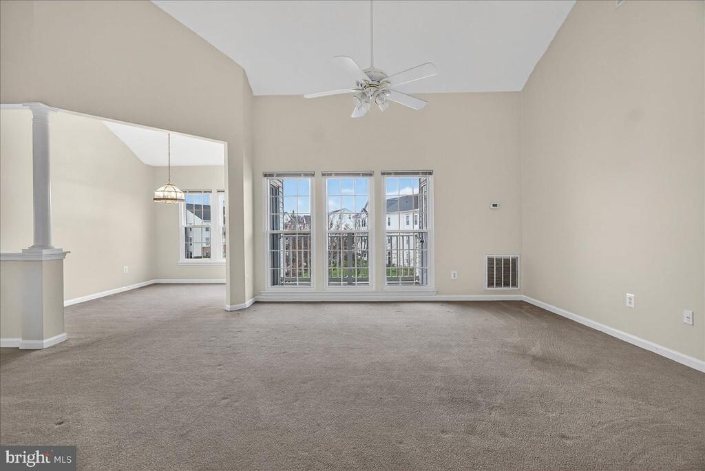 Empty living room with a vaulted ceiling, ceiling fan, and three tall windows.